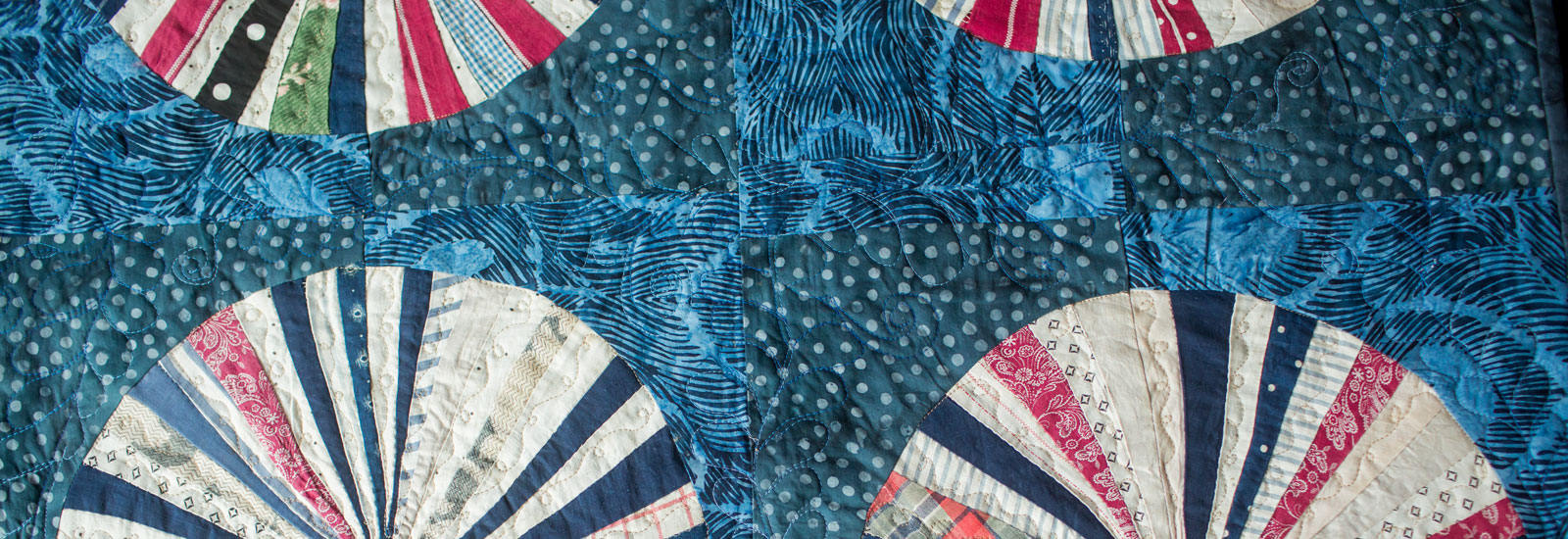 Photo of Diane Murtha posing in front of one of her quilts, which features a pattern of blue diamonds over a white background